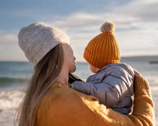 Madre abraza a su bebé en la playa, disfrutando de un momento de paz. Un respiro merecido, como una excedencia y vacaciones no disfrutadas, antes de volver a la rutina.