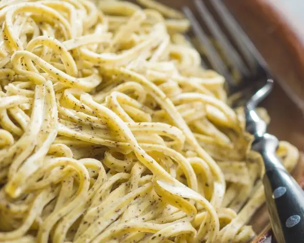 Un primo piatto invitante di tagliolini al limone, conditi con una salsa cremosa e profumata, pronti per essere gustati con una forchetta.