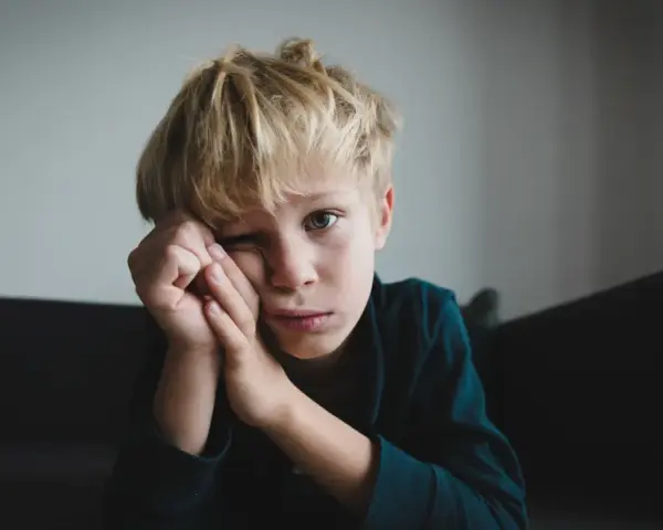 Chłopiec z blond włosami, zamyślony, opiera głowę na dłoniach. Może to być obraz przedstawiający zespół Aspergera – objawy u nastolatków, takie jak trudności w komunikacji.