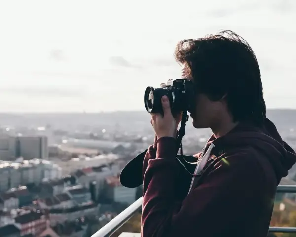 Młody mężczyzna z aparatem w rękach, uchwycony w kadrze z widokiem na miasto. Jego wzrok skupiony jest na obiektywie, jakby chciał uwiecznić piękno chwili za pomocą viewnx 2.