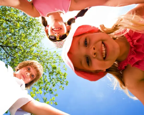 Trois enfants souriants, vus d'en bas, profitent d'une journée ensoleillée lors d'un camp sportif.
