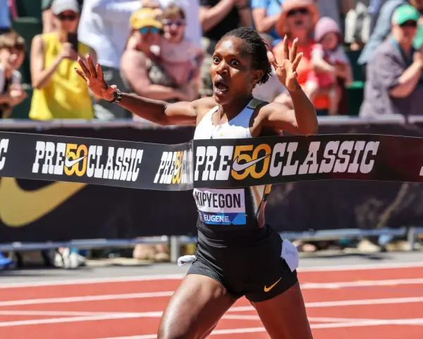 Faith Kipyegon przekracza linię mety z uniesionymi rękami, triumfując na bieżni.