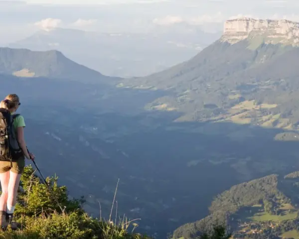 Randonneuse contemplant un panorama grandiose lors d'une traversée de la Chartreuse. Les montagnes s'étendent à perte de vue.