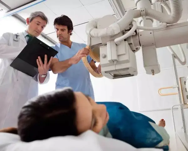 Lekarz i technik elektroradiolog omawiają badanie RTG pacjentki leżącej na stole.