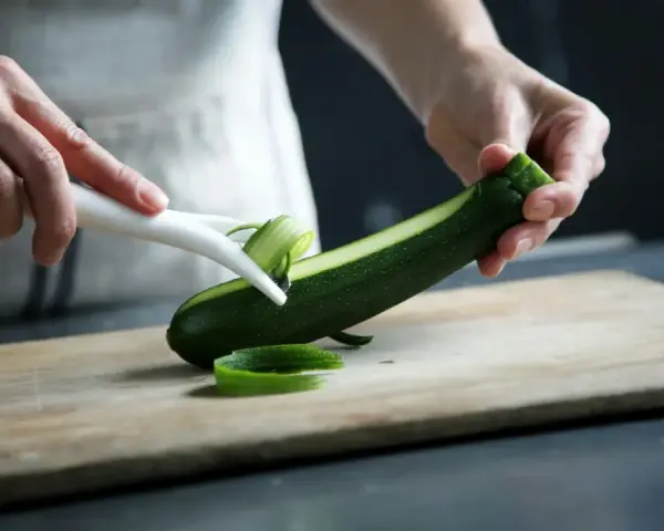 Manos pelando un calabacín para preparar deliciosas recetas con calabacín.