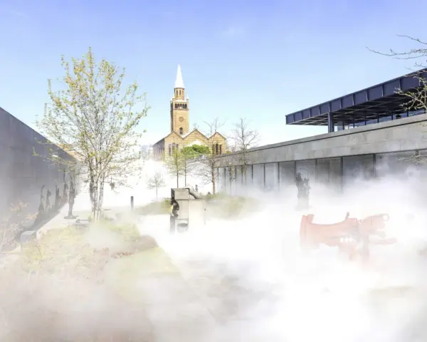 Ein nebliger Garten mit Skulpturen und einer Kirche im Hintergrund, ein friedlicher Ort für Christi Himmelfahrt in Berlin.