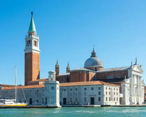 Il campanile di Venezia si erge maestoso accanto alla chiesa con la cupola, mentre barche a vela attendono sul canale.