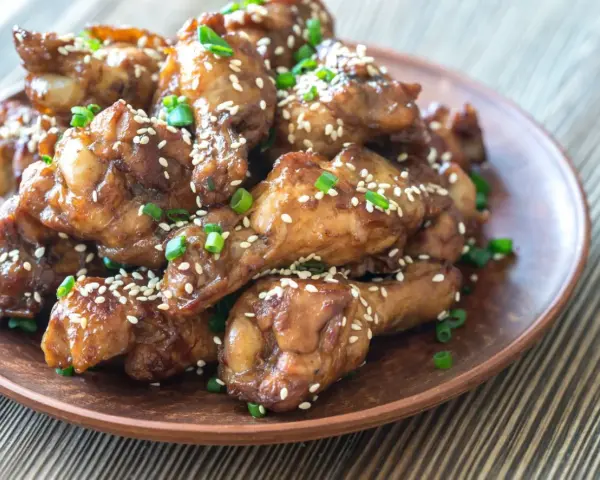 Alitas de pollo glaseadas con sésamo y cebolleta en un plato marrón.