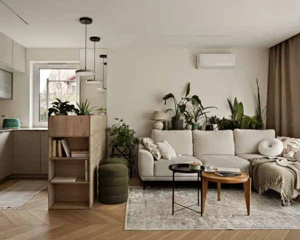 Minimalistyczne wnętrza z dużą ilością zieleni. Jasna kanapa, drewniane meble i kuchnia w neutralnych kolorach tworzą przytulną atmosferę.