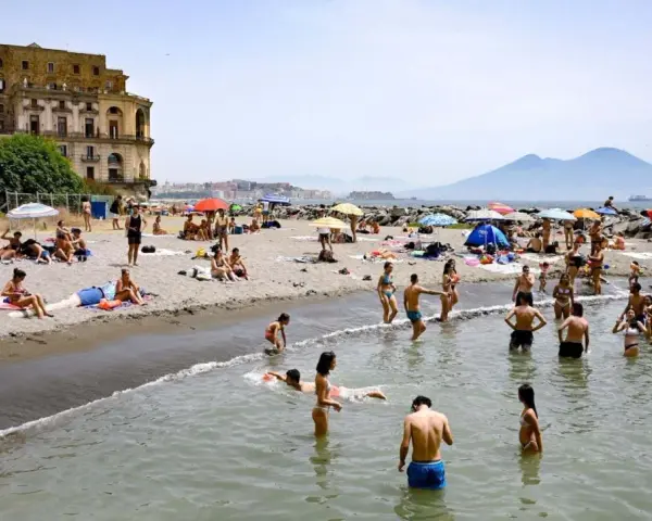 Gente che si gode il sole e il mare sulle spiagge libere di Napoli, con il Vesuvio sullo sfondo.