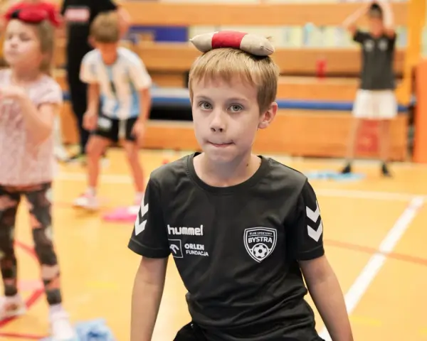 Chłopiec z zabawką na głowie, w koszulce KS Bysstra, podczas zajęć sportowych.