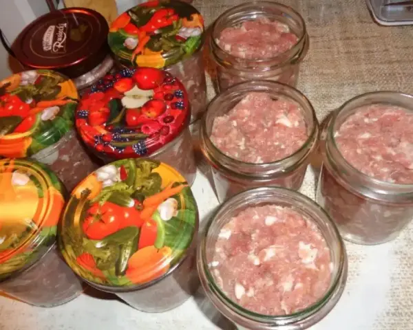 Słoiki z mielonym mięsem, gotowe do pasteryzacji. To pierwszy krok, jak zrobić kiełbasa w słoiku z galaretką. Kolorowe nakrętki z warzywami i owocami.
