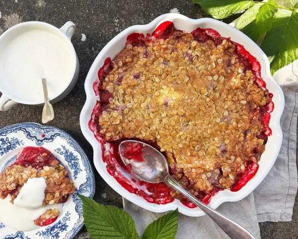En härlig hallonpaj smulpaj med krispig topping, serverad med vaniljsås. Perfekt sommarfika!