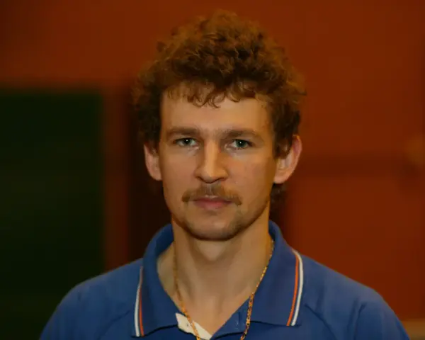 Tomasz Wronka, z kręconymi włosami i wąsami, w niebieskiej koszulce polo.