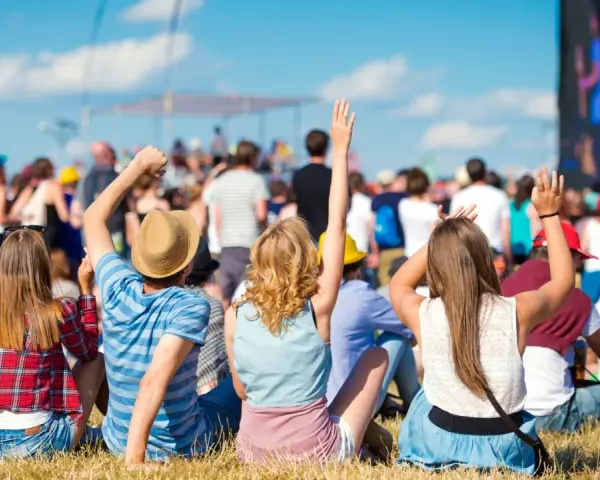 Widok zza pleców na tłum ludzi bawiących się na jednym z letnich festiwali w Polsce. Słońce świeci, niebo jest błękitne.