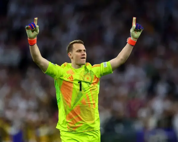 Manuel Neuer, bramkarz w neonowożółtej koszulce z numerem 1, świętuje zwycięstwo, unosząc ręce w geście triumfu.