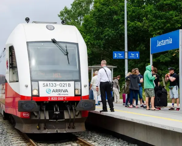 Pociąg Arriva z napisem HEL czeka na pasażerów w Jastarni. Ludzie z bagażami stoją na peronie, gotowi do podróży z Helu do Gdańska.
