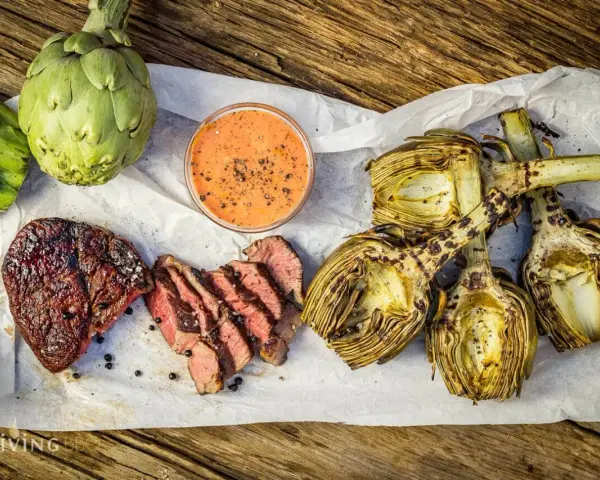 Saftiges Steak und gegrillte Artischocken mit Dip auf Holzuntergrund.