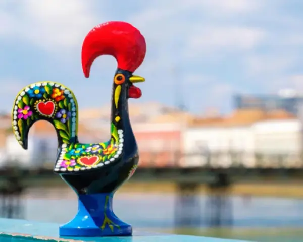Un gallo de cerámica negro, decorado con flores y corazones, se alza orgulloso con su cresta roja.