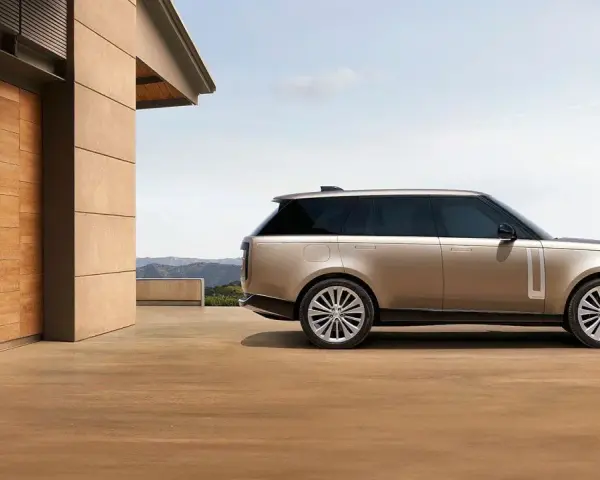 Elegancki Range Rover w kolorze piaskowym, zaparkowany przed nowoczesnym domem z drewnianymi drzwiami. Sprawdź range rover cena!