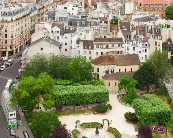 Vista aérea de un barrio latino con edificios antiguos, calles estrechas y un parque verde con gente disfrutando del día.