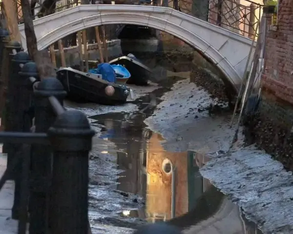 Canali di Venezia quasi asciutti, con barche arenate e riflessi di palazzi. Si vede quanto sono profondi i canali di Venezia in questa situazione insolita.