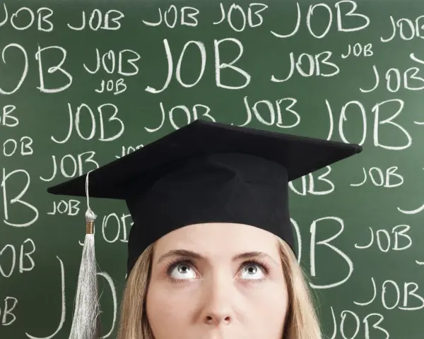 Absolventin mit Doktortitel blickt nach oben, während die Tafel voller "JOB" steht. Die Suche nach Arbeit nach dem Studium ist intensiv.