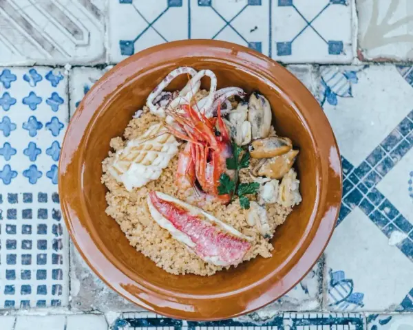Un saporito cous cous di pesce con gamberi, calamari, cozze e triglia, guarnito con prezzemolo fresco.