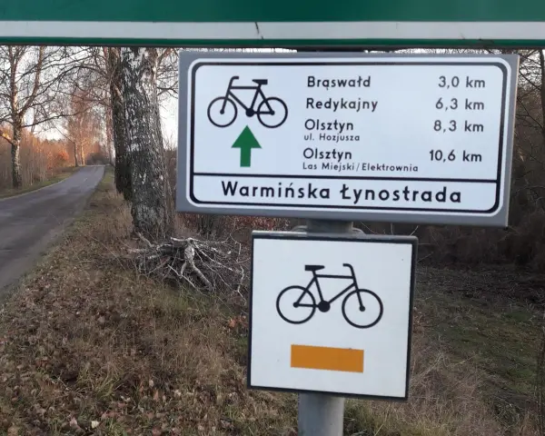Znak drogowy informuje o odległościach do Brąswałd, Redykajn, Olsztyna i Lasu Miejskiego. To część szlaku Warmińska Łynostrada.
