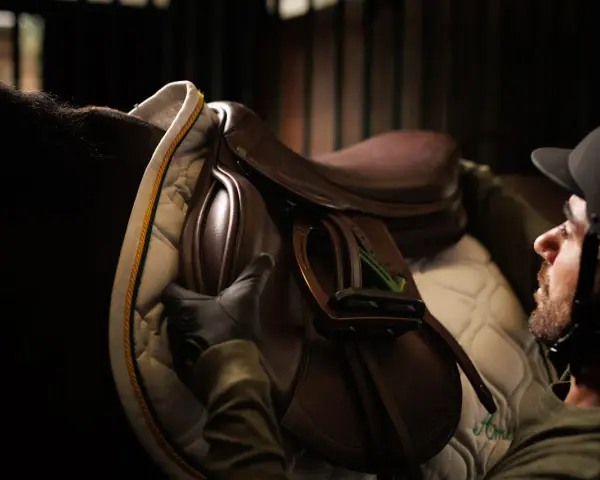 Un cavalier ajuste une selle Amerigo Sellier sur un cheval.