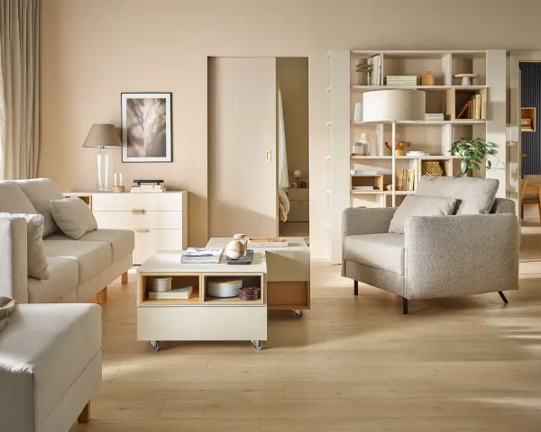 Nowoczesny salon po przemeblowaniu pokoju. Jasne meble, sofa, fotel, stolik kawowy i regał tworzą przytulną przestrzeń.