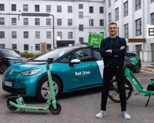 Ein Mann steht stolz neben einem Bolt Drive Auto, E-Scooter und Fahrrad. Er ist ein Bolt Fahrer, der umweltfreundliche Mobilität fördert.