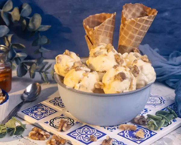 Schüssel mit Eiscreme, garniert mit Nüssen und Honig. Ein Glas Honig und Waffelhörnchen im Hintergrund. Ein süßer Genuss: Eis mit Honig statt Zucker.