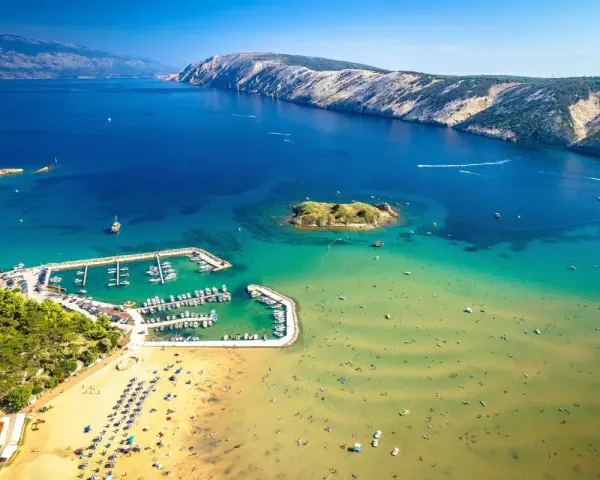 Piaszczyste plaże w Chorwacji, z turkusową wodą, łodziami w marinie i ludźmi cieszącymi się słońcem.