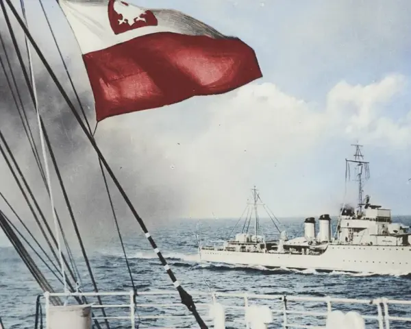 ORP Wicher płynie po wzburzonym morzu. Na pierwszym planie widać fragment statku i polską flagę.
