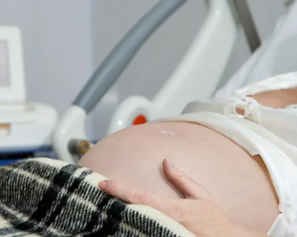 Brzuch kobiety w ciąży, ręka na brzuchu, monitor KTG i łóżko szpitalne.