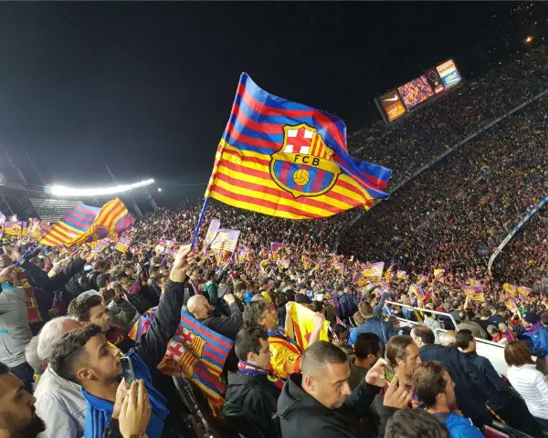 Tłum kibiców na stadionie unosi flagi z herbem FC Barcelona. Flaga Katalonii powiewa dumnie nad głowami fanów.