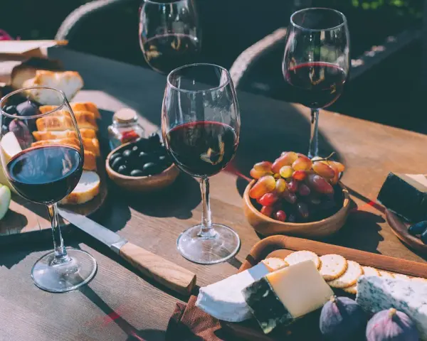 Degustacja wina merlot: jakie to wino? Kieliszki pełne rubinowego trunku, deska serów, winogrona, oliwki i figi tworzą idealną kompozycję.