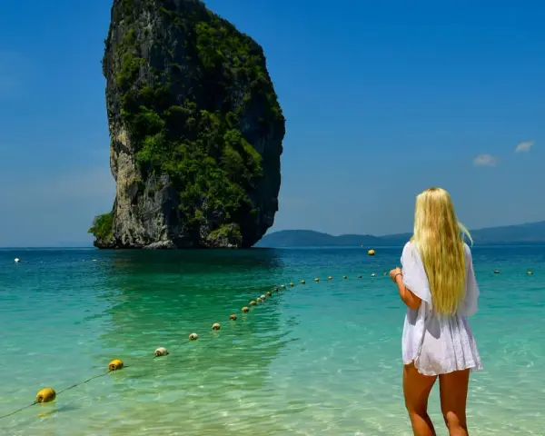 Blondynka podziwia egzotykę tropikalnej wyspy z turkusową wodą i skalistą formacją w tle.