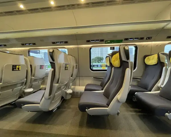 Wnętrze pociągu Pendolino z rzędami szarych foteli z żółtymi zagłówkami.