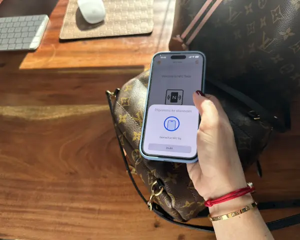 Dłoń trzymająca telefon z aplikacją NFC nad torebką Louis Vuitton.