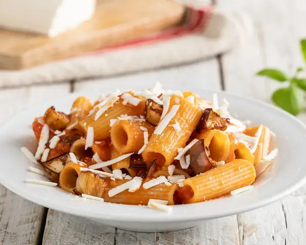 Piatto di pasta alla norma con rigatoni, melanzane fritte, pomodoro e ricotta salata grattugiata.