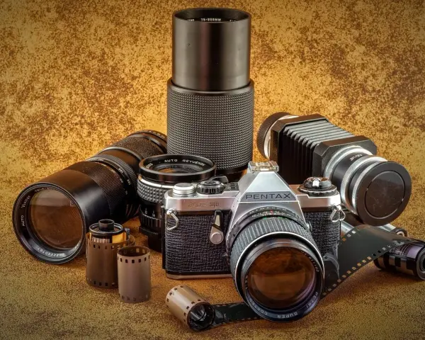 Kolekcja różnych rodzajów aparatów fotograficznych i akcesoriów, w tym aparat Pentax, obiektywy i klisze.