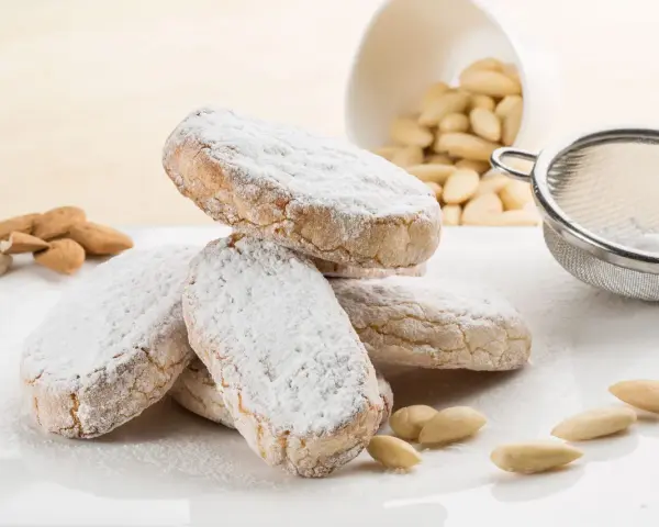 Dolce di Siena cosparso di zucchero a velo, con mandorle e setaccio sullo sfondo.