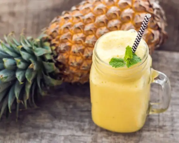 Orzeźwiający koktajl z ananasa i banana, ozdobiony miętą, na drewnianym tle.