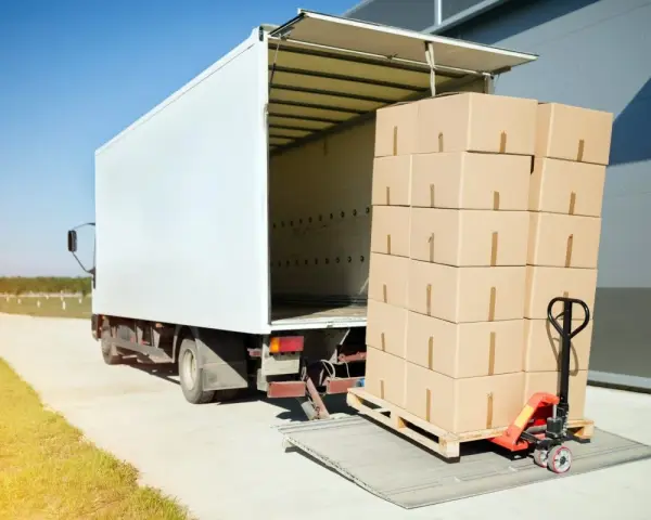 Stos kartonów na palecie, gotowy do załadunku do białej ciężarówki. Ubezpieczenia cargo chronią takie przesyłki.