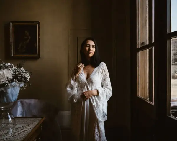 Kobieta w białej sukni, obok bukiet kwiatów. Scena sugeruje przygotowania do ślubu za granicą, co wyjaśnia przyczyny popularności wesel typu "destination wedding".