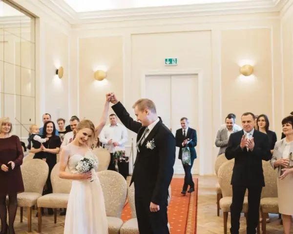 Para młoda świętuje swój ślub cywilny, trzymając się za ręce. W tle widać gości i rodzinę.