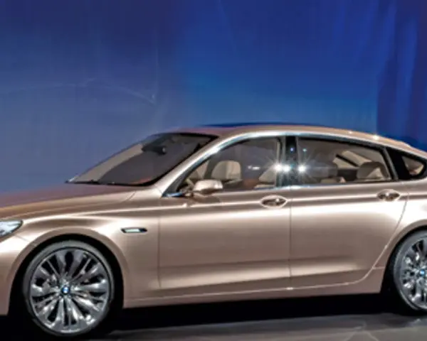 Eleganckie, złote bmw gt z przyciemnianymi szybami i chromowanymi felgami stoi na tle niebieskiej ściany.