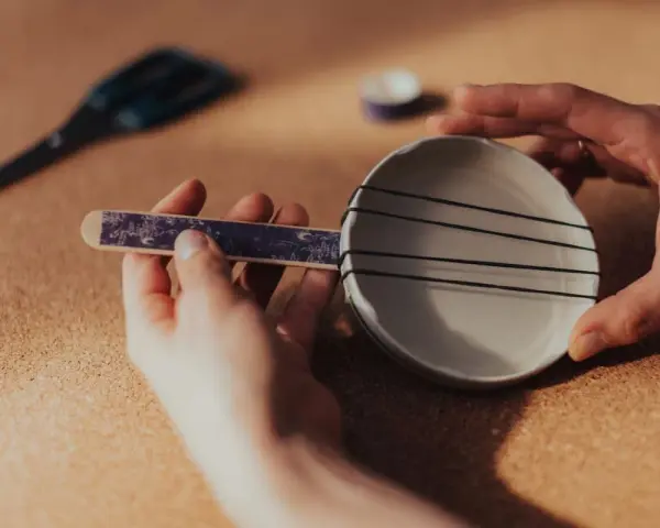 Jak zrobić instrument muzyczny do szkoły? Ręce składają prosty instrument z talerzyka, gumek i patyczka.